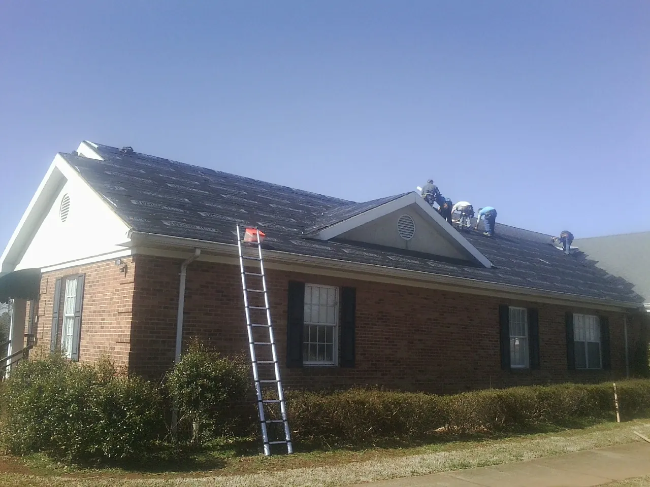 Crew tearing shingles off a brick ranch roof with a ladder set — Metal Roof Repair work by our crew in Norway